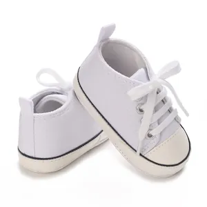 Close-up of white infant canvas sneakers with soft soles and lace-up design.