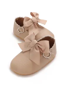 Close-up of beige baby girl princess shoes with large ribbon bows and scallop trim.