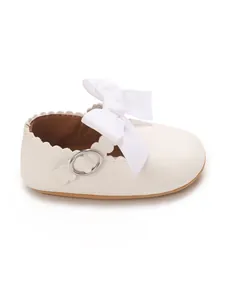 Macro detail of white baby girl princess shoe featuring a large bow and elegant scalloped edge