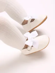 Close-up of white baby princess walking shoes with decorative bow and scalloped edges