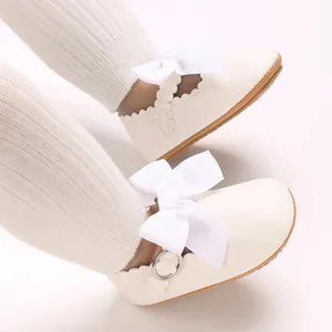 Close-up of white baby Mary Jane shoes featuring elegant bow details and scalloped edges