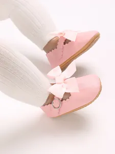 Detail showing soft pink PU baby princess shoes with a bow and scalloped edge.