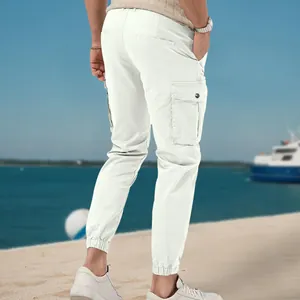 Men's white multi-pocket cargo jogger pants in a stylish beach outdoor setting.