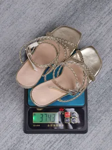 Detail showing gold metallic strappy square-toe sandals on a digital weight scale