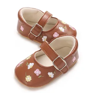 Detail von braunen Baby-Mary-Janes mit zarter Blumenstickerei und silberner Schnalle.