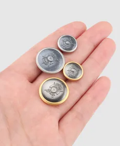 Detailed view of vintage brass metallic buttons with crest design on a hand for scale.
