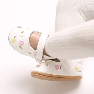 Detailansicht der weißen Baby-Mary-Jane-Schuhe mit Blumenstickerei und Gummisohlen.