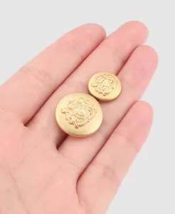 Detailed close-up of gold brass buttons with royal heraldic engraving held in a palm