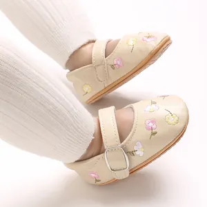 Detailaufnahme von beigen Baby-Mary-Janes mit bunter Blumenstickerei und Riemen.