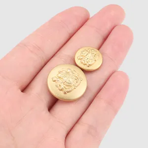 Golden brass blazer buttons set with embossed crest design held in hand for scale