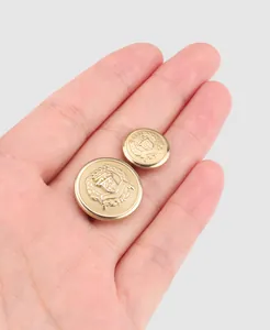 Primer plano de botones de latón dorado con escudo en relieve, sostenidos para la escala.