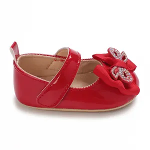 Side view of red patent leather baby shoes featuring a rhinestone bow and Velcro strap