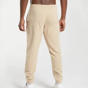 Rear view of beige men's loose fit knitted joggers with cuffed ankles on a model