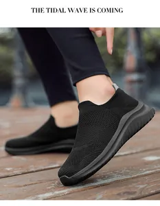 Detailed shot of black fly-knit slip-on sneakers worn by a model on wooden deck.