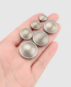A close-up view showing various sizes of round brass metal buttons with linear texture on a hand