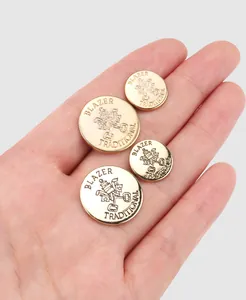 Close-up of gold metal blazer buttons with traditional crest engraving held in hand.