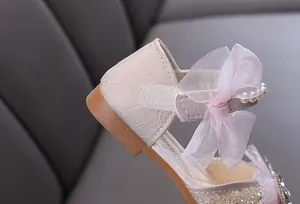Detalle de elegantes zapatos de princesa rosa para niña con lazo de encaje y perlas.