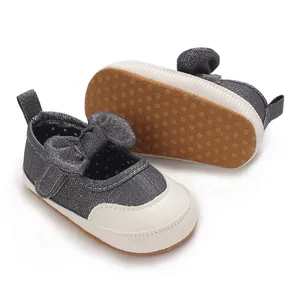 Close-up of grey denim baby shoes with a white toe cap, bow detail, and non-slip rubber dotted sole