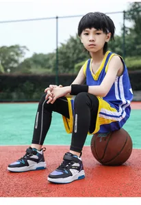 Détail d'un garçon portant des baskets montantes assis sur un ballon de basket