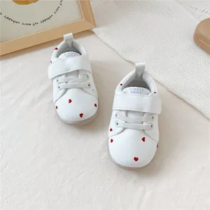 Detailopname van witte baby loopschoentjes met rode hartjes en klittenbandsluiting