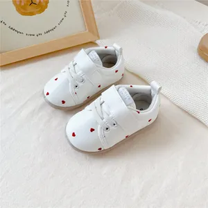 Close-up van witte baby loopschoentjes met een rood hartjespatroon en klittenband