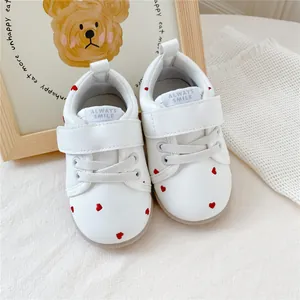 Detail van witte baby loopschoenen met rode hartpatronen en klittenbandsluiting.