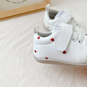 Detail van witte baby loopschoenen met rode hartjes borduursels en klittenbandsluiting