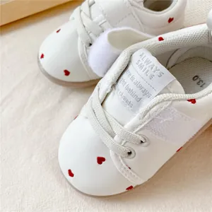 Detailweergave van witte babyloopschoenen met rode hartjes en een zachte zool