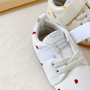 Close-up detail van witte baby loopschoen met rode hartjespatronen en klittenband