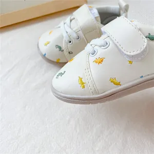 Detailopname van crème baby-loopschoentjes met kleurrijke dinosaurusborduringen