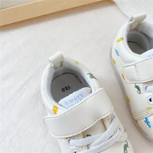 Detail van beige babyloopschoenen met dinosauruspatroon en klittenbandsluiting