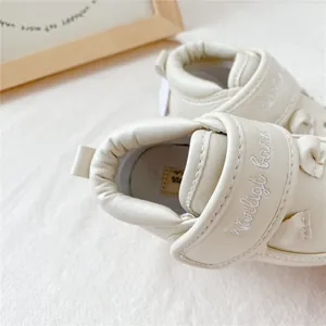 Gros plan de chaussures de marche pour bébé crème avec broderie et cuir souple.