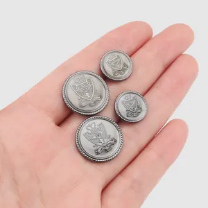 Boutons métalliques vintage avec blason sur une main, montrant différentes tailles