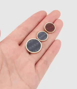 Detailed view of checkered resin buttons in various sizes held in hand for scale