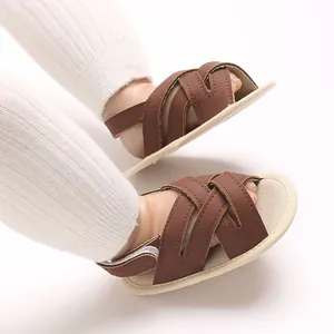 Primer plano de sandalias para bebé de cuero PU marrón con tiras cruzadas y suela blanda.