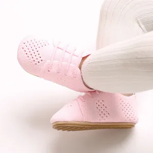 Close-up detail of pink knitted baby shoes with hollow-out design and soft soles.