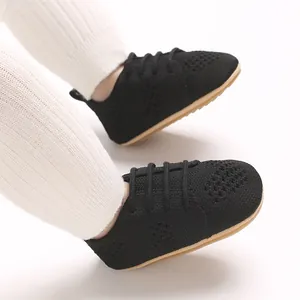 Detail view of black hollow-out knit infant shoes paired with white ribbed leggings