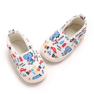 Primer plano de zapatos de suela blanda para bebé con patrones de dinosaurios y coches