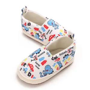 Primer plano de zapatos de bebé blancos con coloridos estampados de dinosaurios y vehículos.