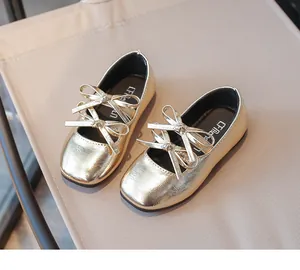 Detailed view of shiny gold girls' flat shoes with double bow knots on a beige background