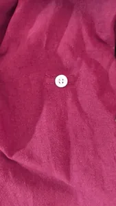 Detailed macro view of a white four-hole button on maroon cotton linen fabric shirt