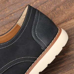 Detalle de zapato de cuero negro con costuras blancas y suela de color beige.