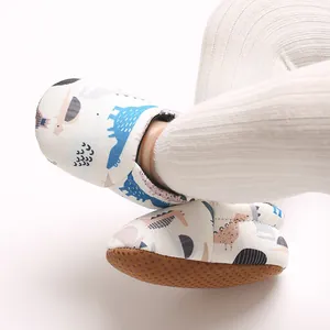 Primo piano di scarpine morbide per neonati con simpatico dinosauro blu su fondo bianco