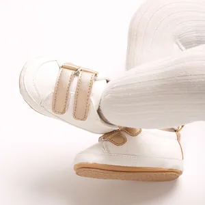 Nahaufnahme weißer PU-Babyschuhe mit goldenem Klettverschluss und weicher Sohle