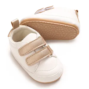 Detailansicht weißer Babyschuhe mit goldenen Klettverschlüssen und weichen braunen Sohlen.