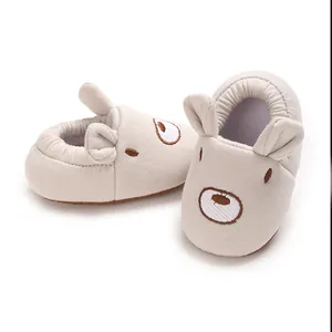 Dettaglio di scarpine da neonato beige con viso d'orso ricamato e orecchie 3D