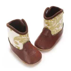 Close-up of baby winter boots with brown leather base and golden floral pattern.