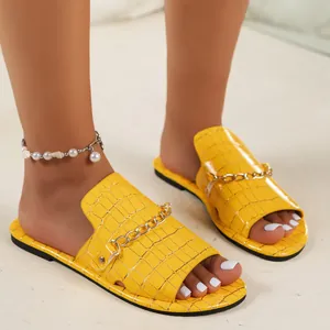 Leuchtend gelbe flache Sandalen in Krokodilleder-Optik mit goldener Kette für den Sommer