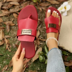 Rote Zehentrenner-Sandalen mit Goldmetall-Akzent in einer Lifestyle-Außenumgebung.