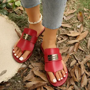 Detailansicht roter Zehentrenner-Sandalen mit gravierter goldener Metallplatte oben